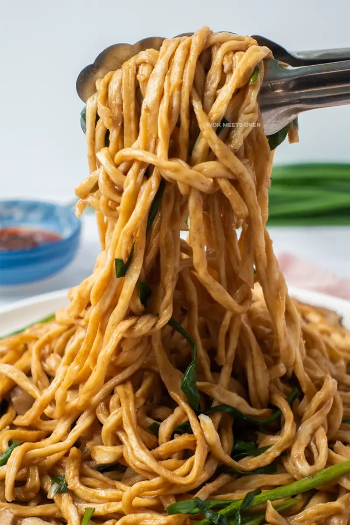 Using tongs to pick up e-fu noodles