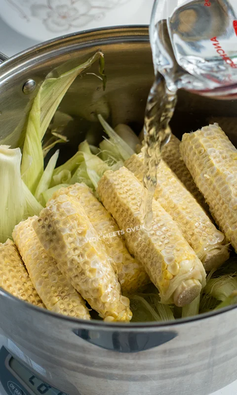 Adding in water into pot full of corn cobs, husks, and silk