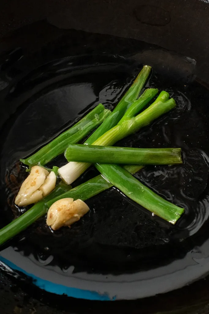 Adding in green onions and crushed garlic to wok