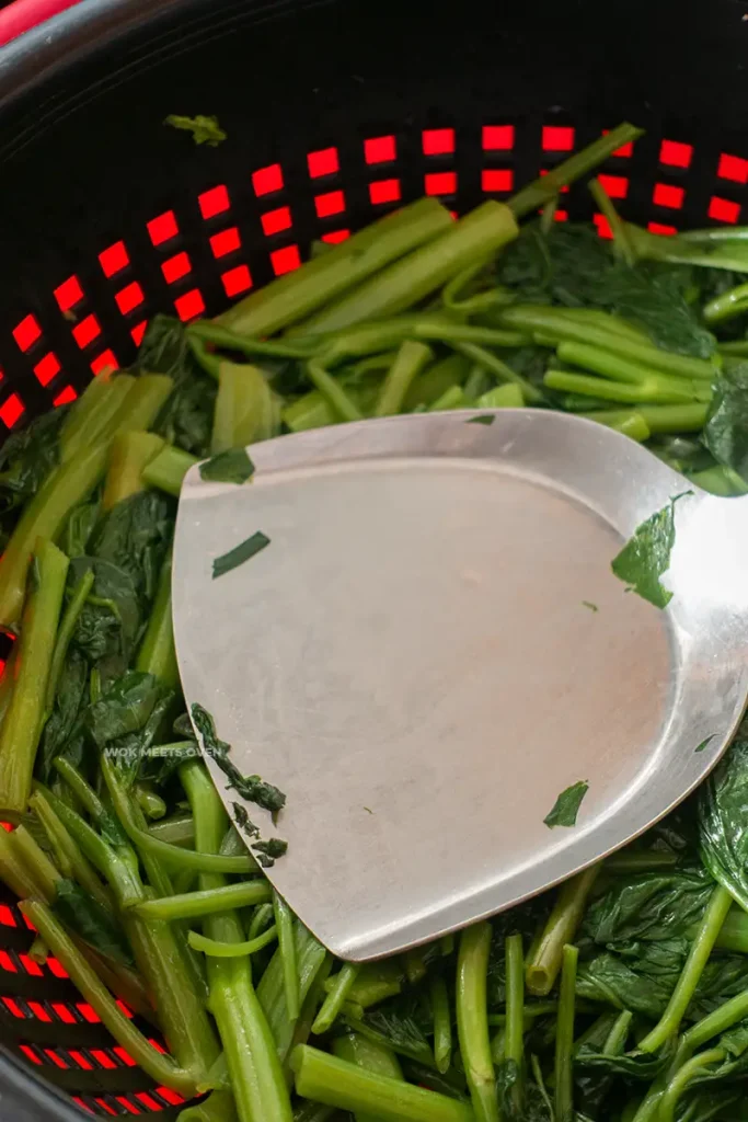 Pressing down on cooked Ong choy to strain out extra water