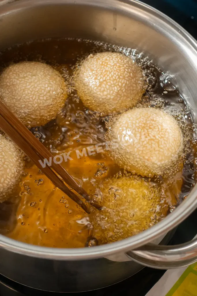 Sesame balls floating and chopsticks pushing them back down into the oil
